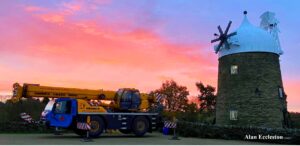 Pink dawn sky frames a large mobile crane resting in front of Heage Windmill, without sails.